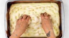 two hands on top of a pan of food that is uncooked and ready to be baked