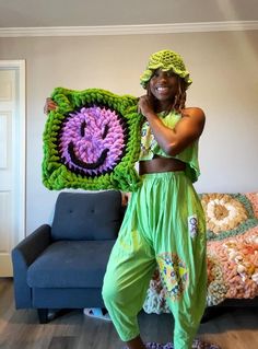 a woman is holding up a crocheted smiley face blanket in her living room