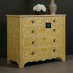 an ornate yellow chest of drawers with flowers on top