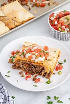 a white plate topped with an enchilada next to a bowl of salsa