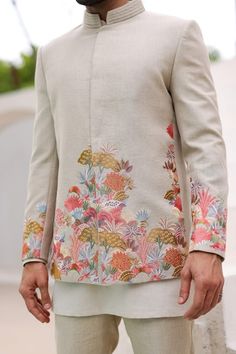 a man standing in front of a building wearing a white suit with colorful flowers on it