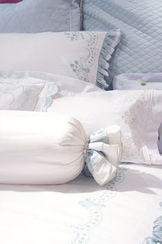 a white bed topped with lots of pillows next to a pillow on top of it