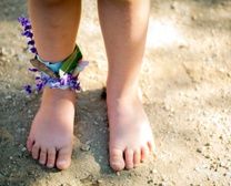 a person standing in the sand with purple flowers on their ankles and barefoot sandals attached to them