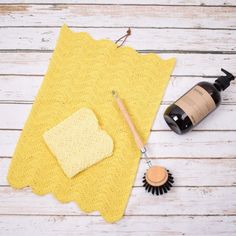 a crocheted yellow towel, bottle and brush on a white wooden table top