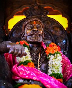 a statue of an old man with flowers around his neck and hands in front of him