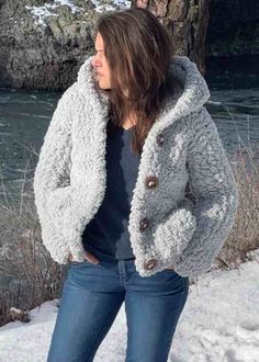 a woman standing in the snow wearing a gray jacket and jeans with her hands in her pockets