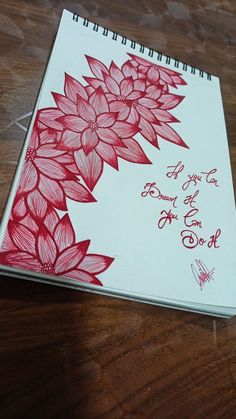 a note book with red flowers on it sitting on top of a wooden table next to a pen