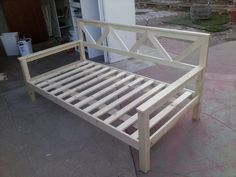 a wooden bed frame sitting on top of a cement floor next to a white building