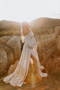 a woman in a white dress is standing on some rocks and looking off into the distance