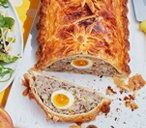 an egg and meat loaf on a plate next to a salad, fork and knife