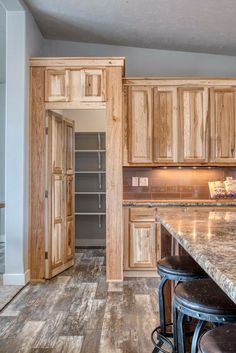 an empty kitchen with wooden cabinets and marble counter tops, stools in front of the island