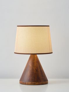 a wooden table lamp with a fabric shade on it's base and a white wall in the background