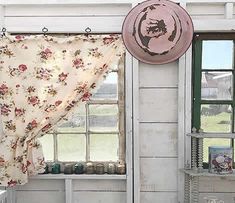 there is a window with a flowered curtain in front of it and a pink hat hanging on the wall