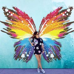 a woman standing in front of a wall painted with a butterfly wings design on it