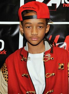 a young boy wearing a red baseball cap and jacket, standing in front of a sign