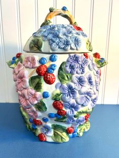 a ceramic teapot with flowers and berries on it sitting on a blue countertop