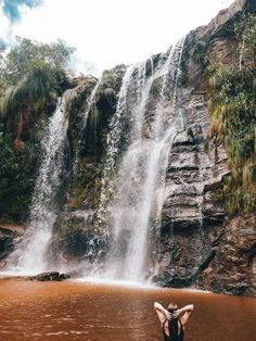 a woman standing in front of a waterfall with her arms up and head above the water