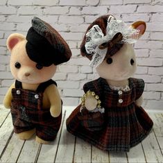 two small teddy bears dressed in brown and black outfits, one wearing a hat and the other with a bow