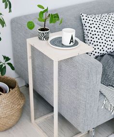 a small table with a coffee cup on it in front of a gray couch and potted plant