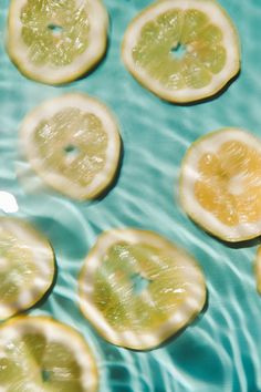 sliced lemons floating in water on top of a blue surface with ripples around them