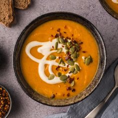 two bowls filled with carrot soup and topped with whipped cream, nuts and pumpkin seeds