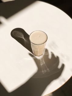 a glass sitting on top of a white table next to a shadow from a person's hand