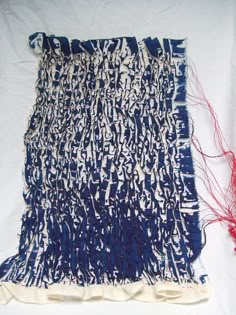 a blue and white piece of cloth next to a red thread on a white surface