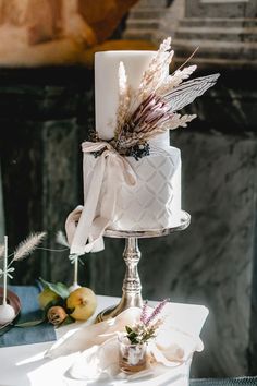 a white wedding cake with feathers on top sitting on a table next to other decorations