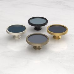 four round knobs with different colors and sizes on white marble counter top, one is gold, the other is black