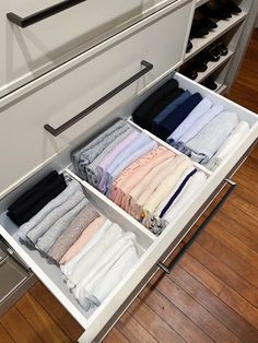 an open drawer with folded clothes in it on a wooden floor next to white drawers