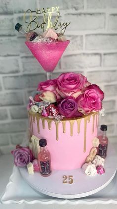 a pink and gold birthday cake with flowers on top, next to a bottle of booze