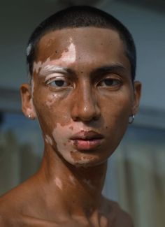 a man with white paint all over his face and chest, looking at the camera