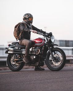 a man riding on the back of a motorcycle down a street next to a bridge