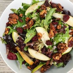 a salad with apples, walnuts and cranberries in a white bowl on a wooden table