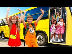 two girls are standing in front of a yellow bus with their hands up and smiling