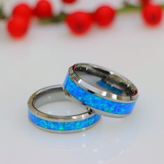 two wedding rings with blue opal inlays on white surface next to red flowers