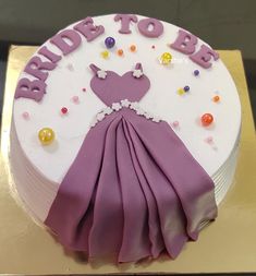 a cake decorated with purple and white icing on a gold platter that says bride to be