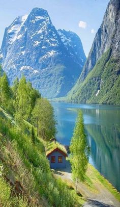 a small cabin on the side of a lake with mountains in the background