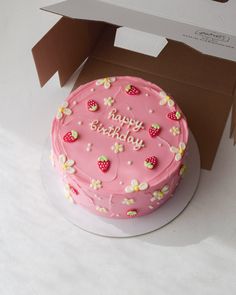 a pink birthday cake with strawberries and flowers on it sitting in a cardboard box