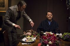 two men standing at a table with food in front of them and one man holding a knife