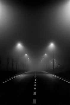 an empty road with street lights in the fog