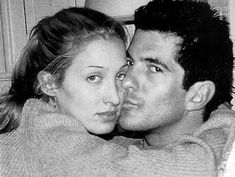 a black and white photo of a young man and woman cuddling in bed together