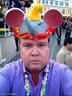 a man wearing a mickey mouse hat with ears on it's head at an amusement park