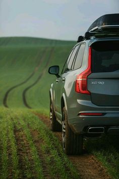 an suv parked on the side of a dirt road in front of a green field