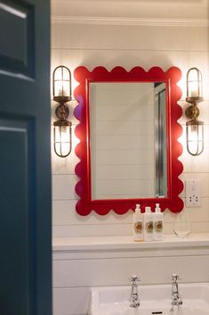 a bathroom sink under a red mirror with lights on it's wall above it