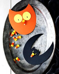 an owl made out of paper sitting on top of a metal plate with candy in it