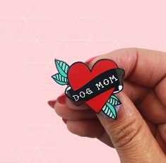 a hand holding a heart shaped pin with the word dog mom on it's side