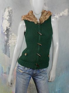 This 1990s European vintage green knit vest zips fully closed in the front to create a high neckline, or you can unzip it to have a more casual look. The stunning vest vest has a faux fox fur hood and brown faux polished horn toggles over the zipper. The honeycomb stitch sweater sleeveless sweater vest has slanted hip pockets with a decorative button on them. The vest is lined in a gray jersey cotton fabric. Brand label: Clockhouse Size: 6 US, 10 UK Material: Acrylic Condition: Excellent ---Meas Cheap Green Sweater Vest For Winter, Cheap Green Sleeveless Sweater, Green Knit Sweater, Vintage Festival, Sleeveless Sweater Vest, Honeycomb Stitch, Fur Hood, Plaid Blazer, 1970s Fashion