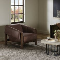 a living room with a chair, table and large window in it's corner