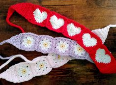 three crocheted headbands with white and red flowers on them sitting on a wooden surface